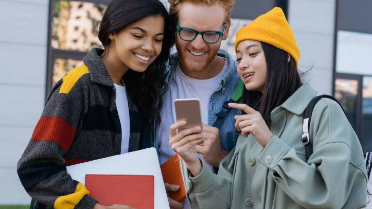 An image of three students, smiling, looking at a mobile phone