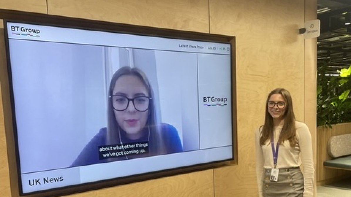Rosie Brown, Chartered Management Degree Apprentice at BT in workpace standing by screen 