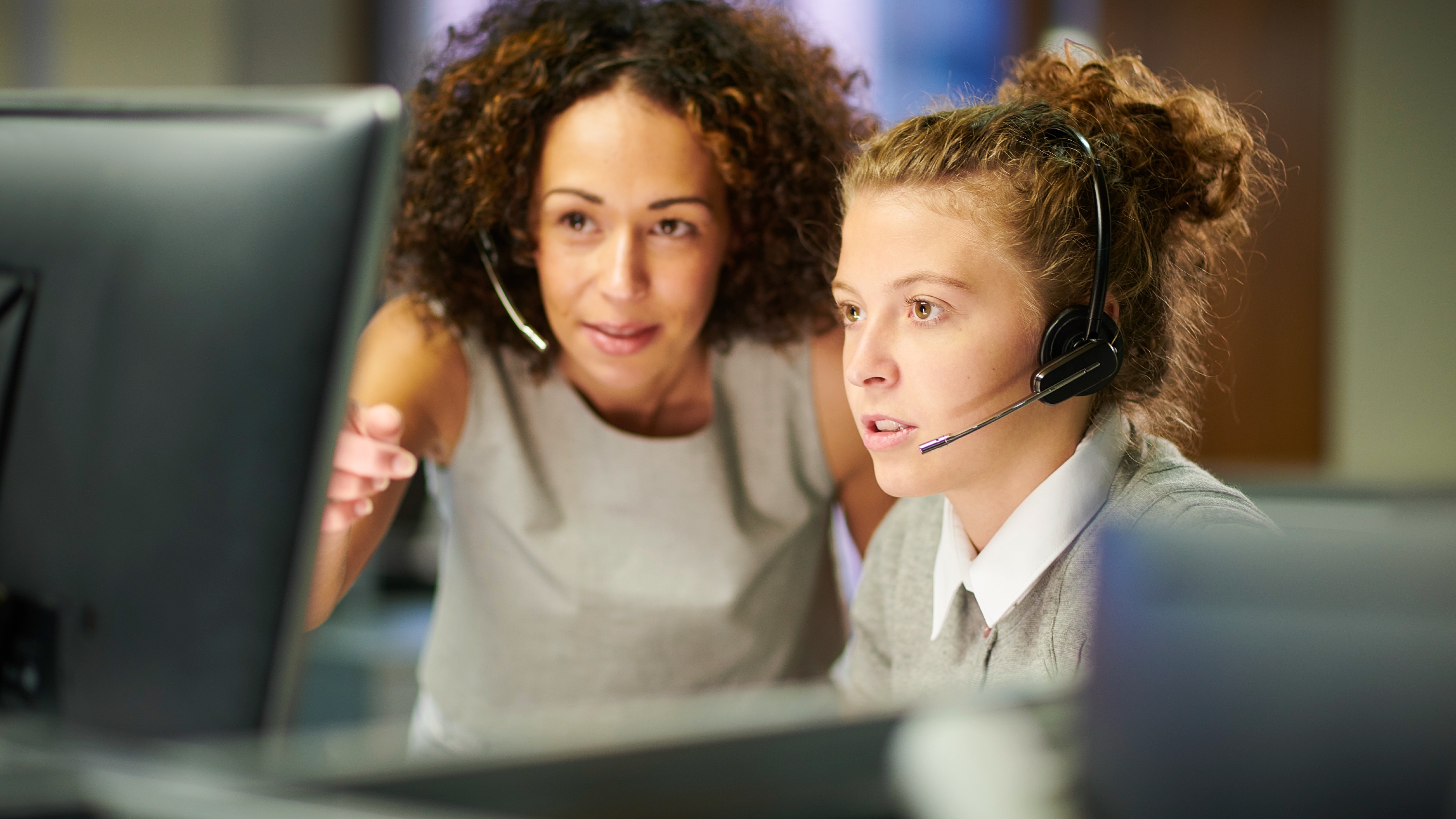 An apprentice wearing a headset is supervised by a team member