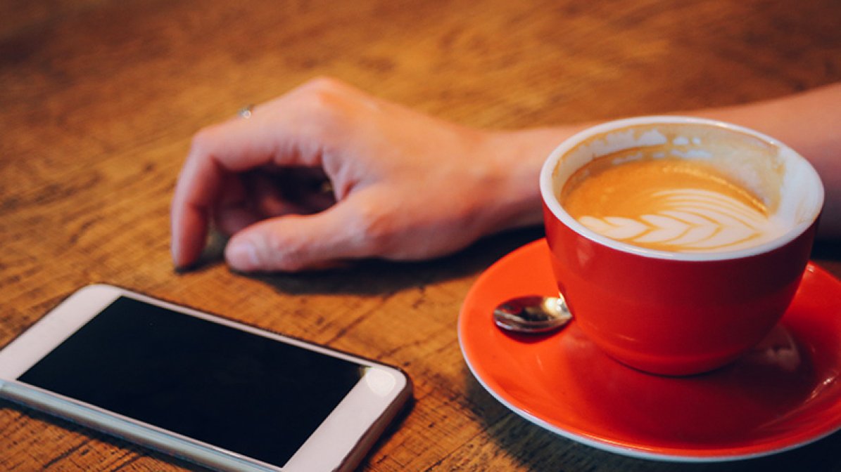 Photo of phone next to a cup of coffee with a person waiting for it to ring