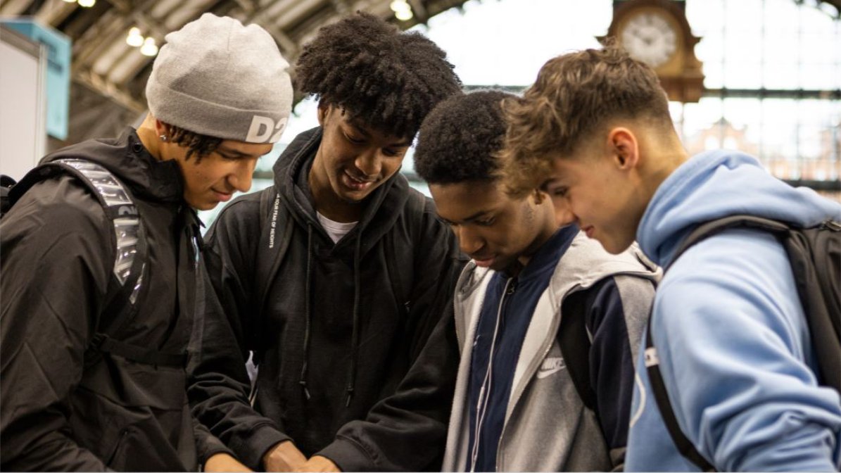 A group of four young people are gathered together, looking at an event map