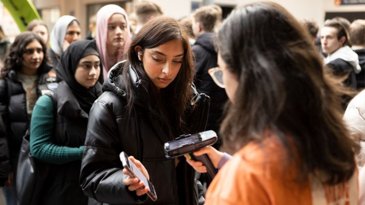A young person entering the UCAS Discover Manchester event is pictured holding up their phone, ready to have their barcode scanned by a member of the UCAS events team, who is holding a scanning device.