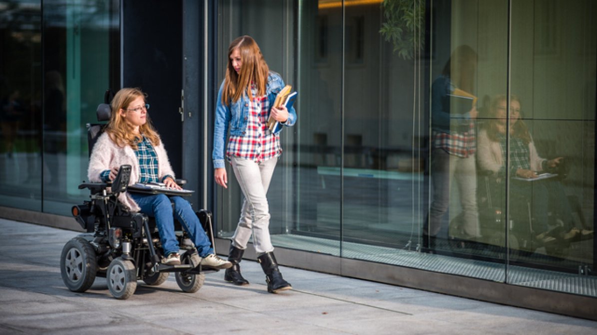 Two students - one using a wheelchair - in university grounds