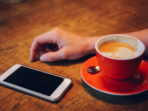 Photo of phone next to a cup of coffee with a person waiting for it to ring